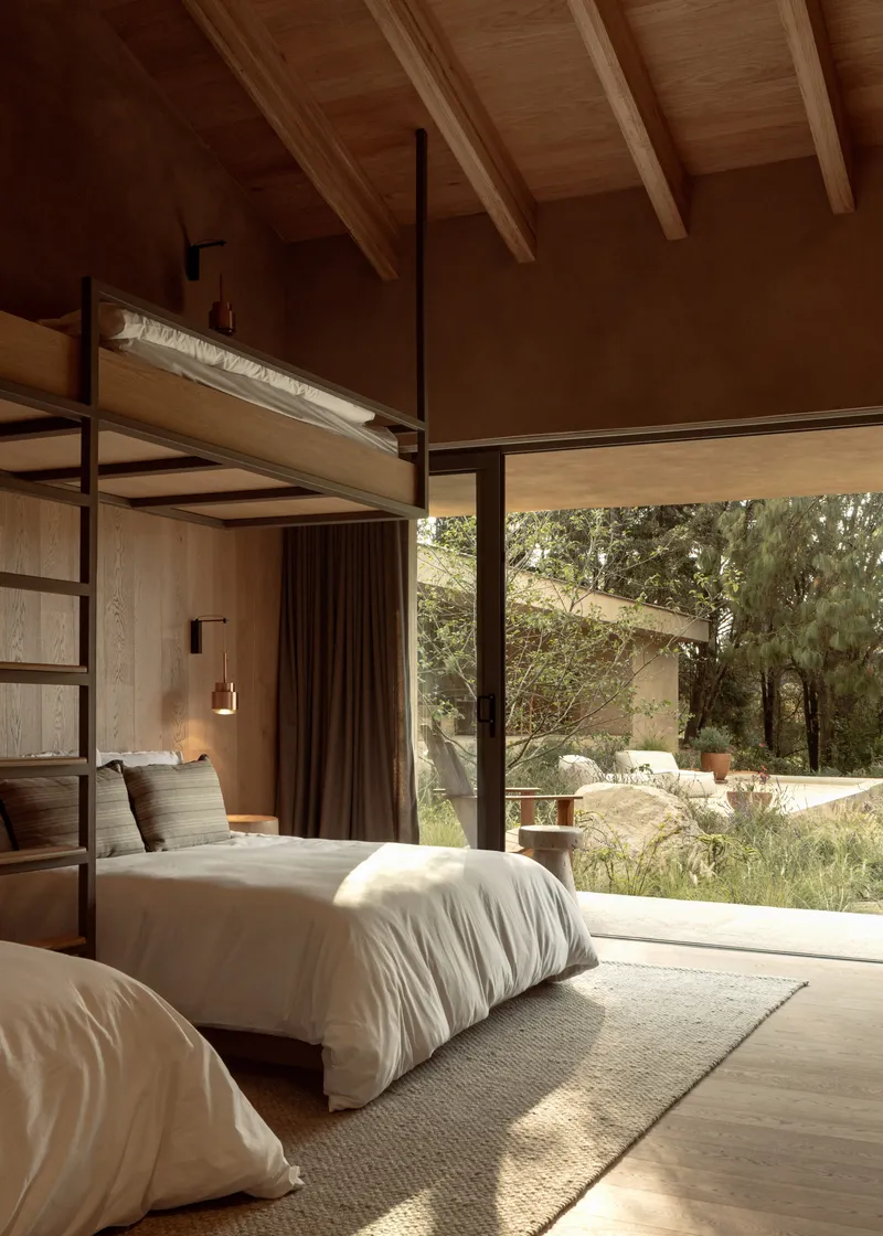 Bedroom with exposed timber ceiling beams and full-height glazing opening to a landscaped garden