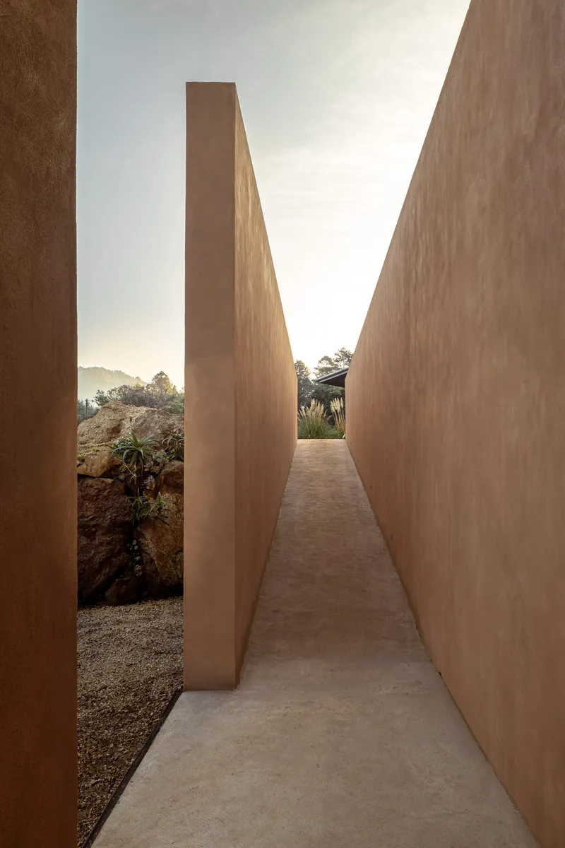 Narrow outdoor corridor between slanted earthen walls under an open sky at dusk