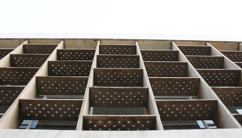 Upward view of the perforated brown panel facade organized in a staggered grid pattern