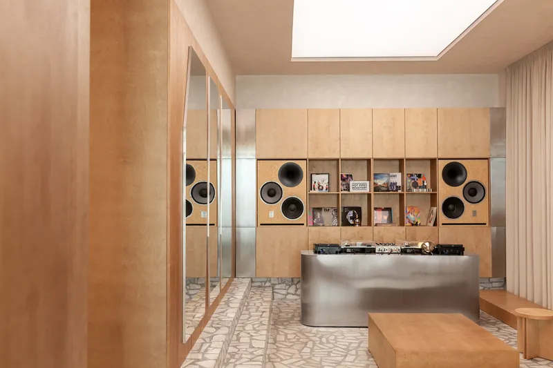 Plywood shelving unit with integrated speakers framing a brushed steel service counter beneath a skylight