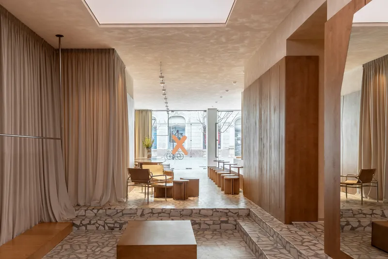 Long interior view through timber columns and floor-to-ceiling curtains toward a storefront window