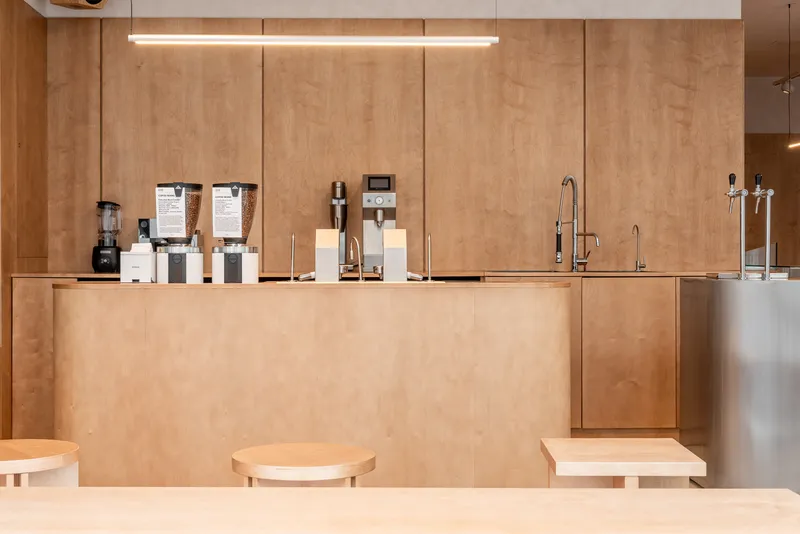 Service counter in plywood with coffee equipment and tap fixtures under linear ceiling lights