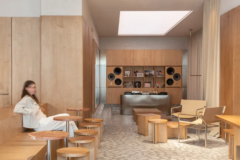 Interior cafe with plywood cabinetry and embedded speakers illuminated by a large skylight overhead