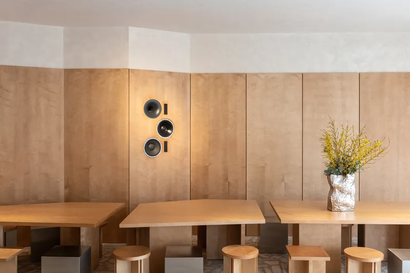 Banquette seating along plywood wall with circular speakers and a vase of yellow flowering branches