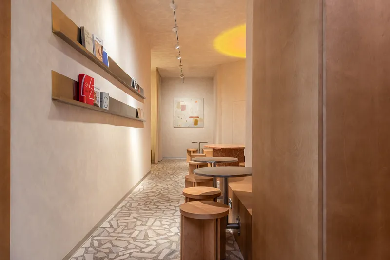 Narrow corridor with terrazzo flooring leading to a framed artwork under warm track lighting