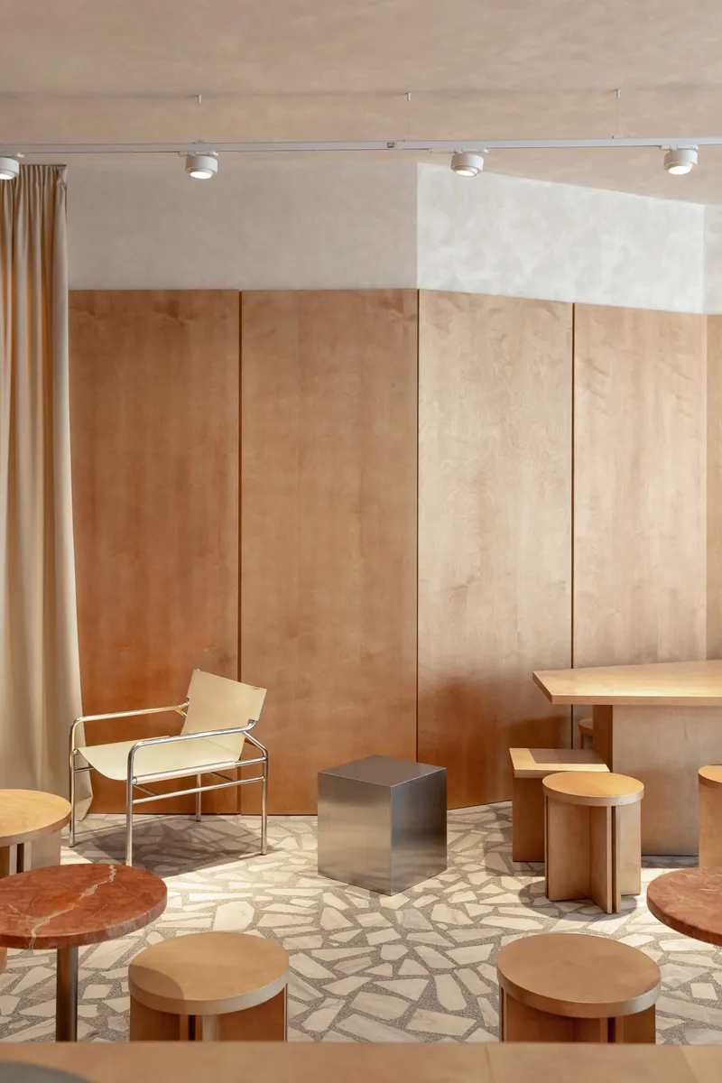 Seating area with plywood wall panels, chrome lounge chair, and terrazzo floor under track lighting