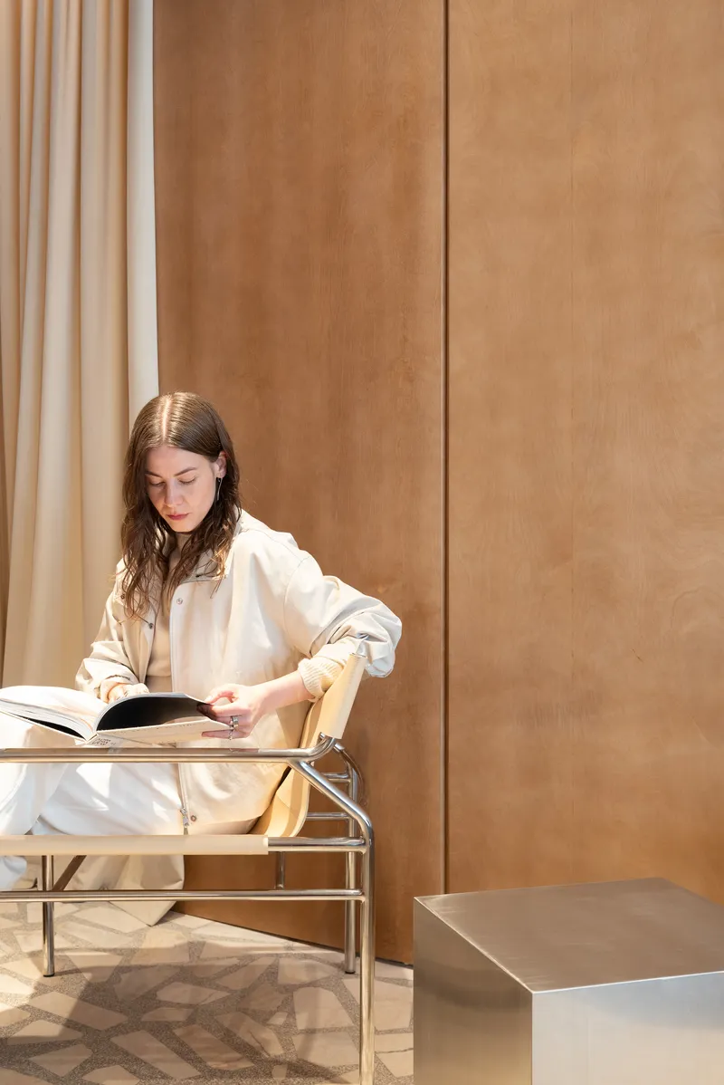 Woman reading at a tubular metal lounge chair against floor-to-ceiling plywood paneling