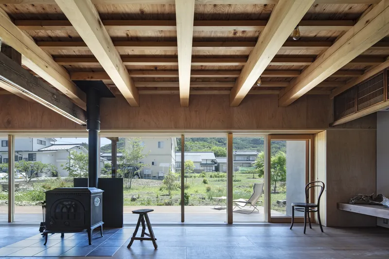 Cast iron wood stove on tile floor beneath exposed timber joists with garden view