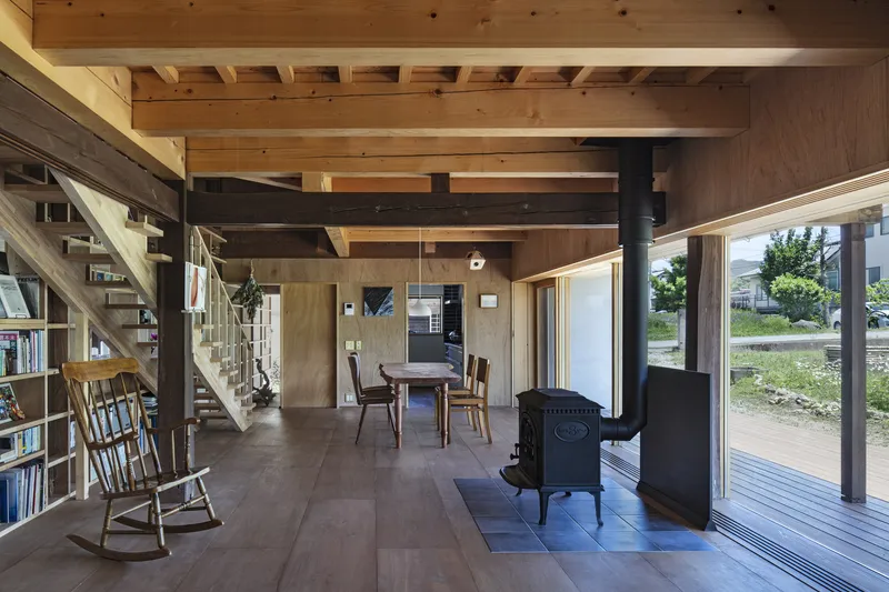 Open-plan interior showing timber staircase, dining area and wood stove with view to exterior landscape through glazing