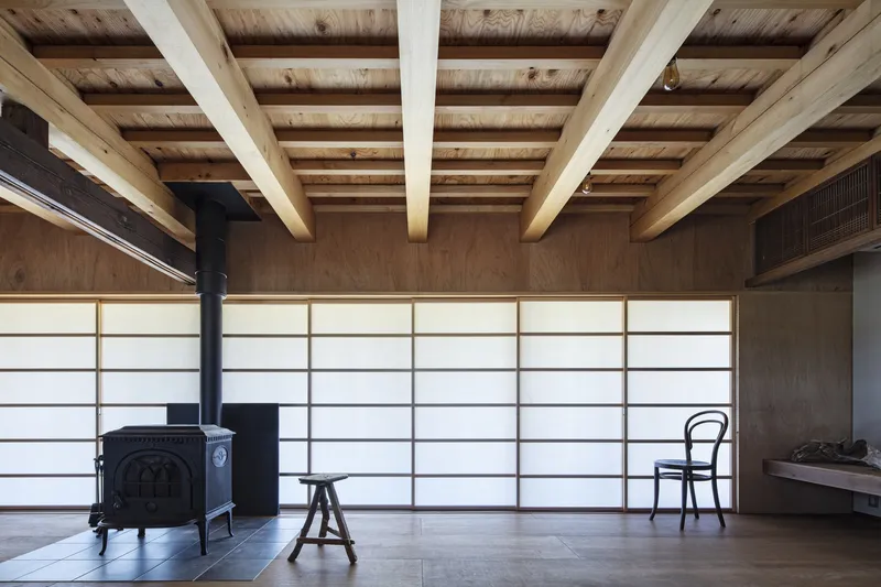 Exposed timber ceiling joists above translucent sliding panels and a cast-iron wood stove on stone tiles