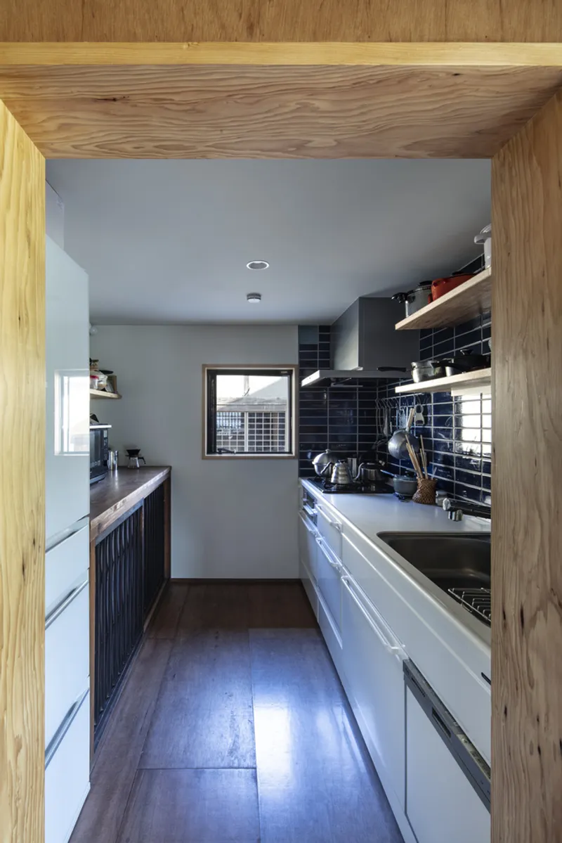 Galley kitchen viewed through timber door frame with black tile backsplash and white lower cabinets
