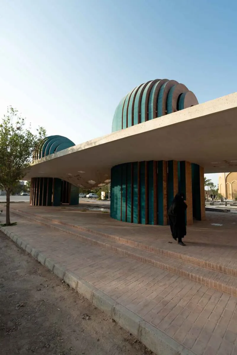 Exterior view of the concrete canopy and teal-tiled barrel vaults at dusk with a pedestrian approaching