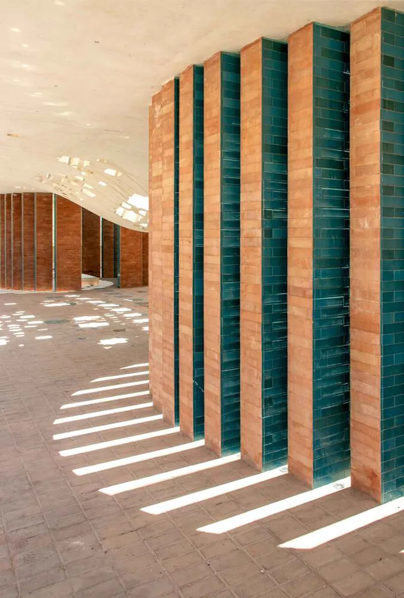 Striped terracotta and teal tile columns casting linear shadows across the tiled floor under the vaulted canopy
