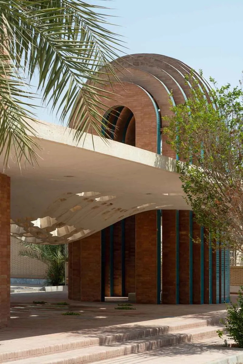 Curved ribbed pavilion with terracotta and teal stripes beneath a concrete canopy and palm fronds