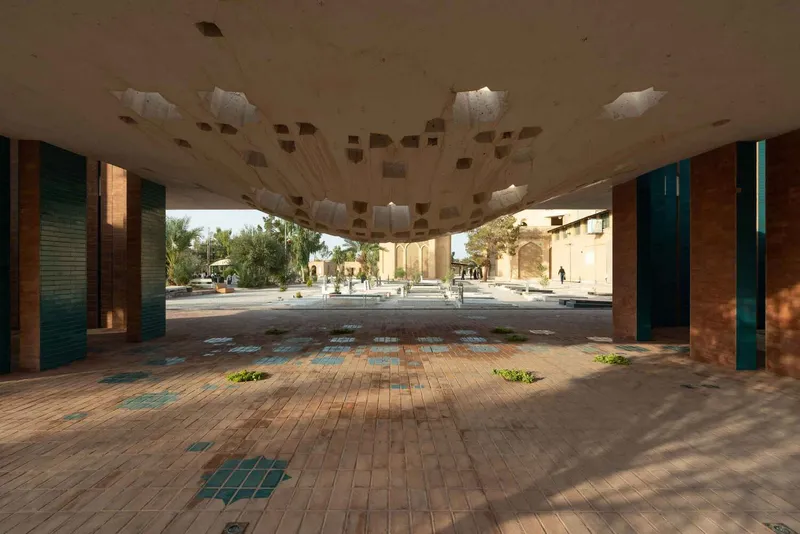 Interior view through the shaded colonnade with patterned brick floor and openings framing the sunlit plaza outside