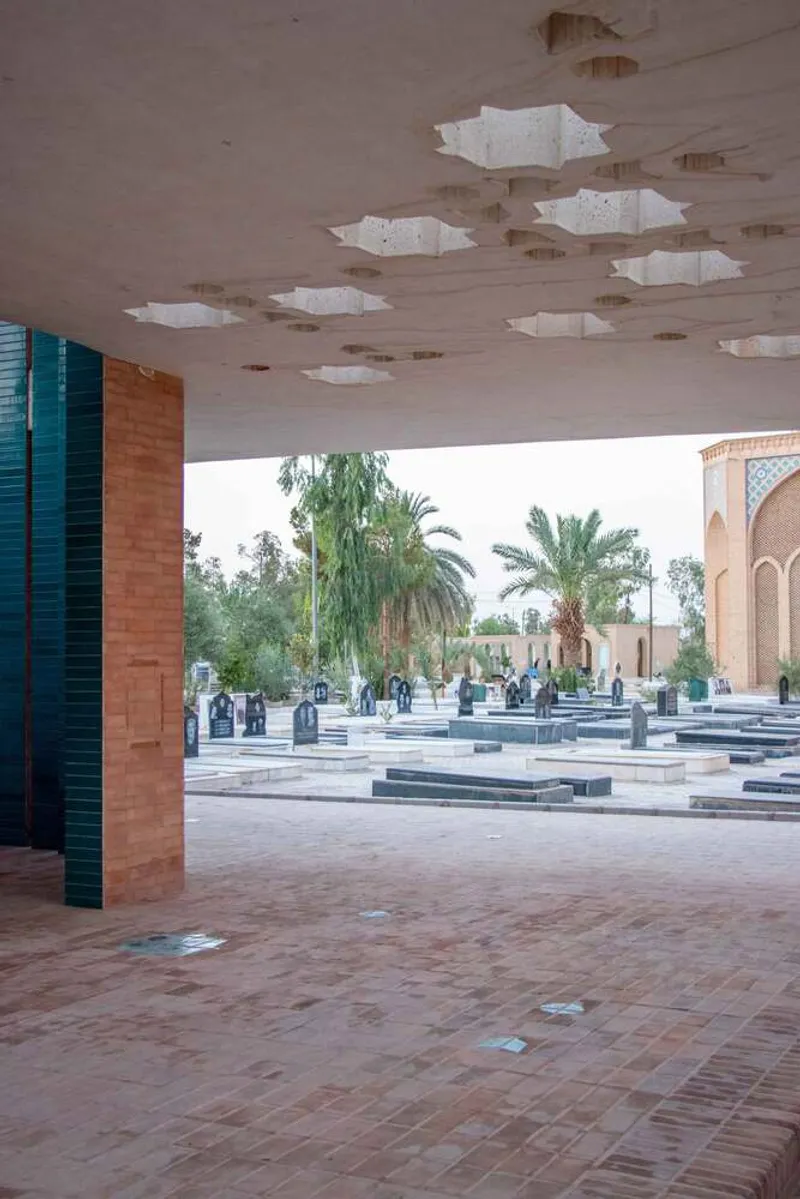 Covered portico with exposed timber ceiling, brick paving, and star-shaped roof openings framing palm trees beyond