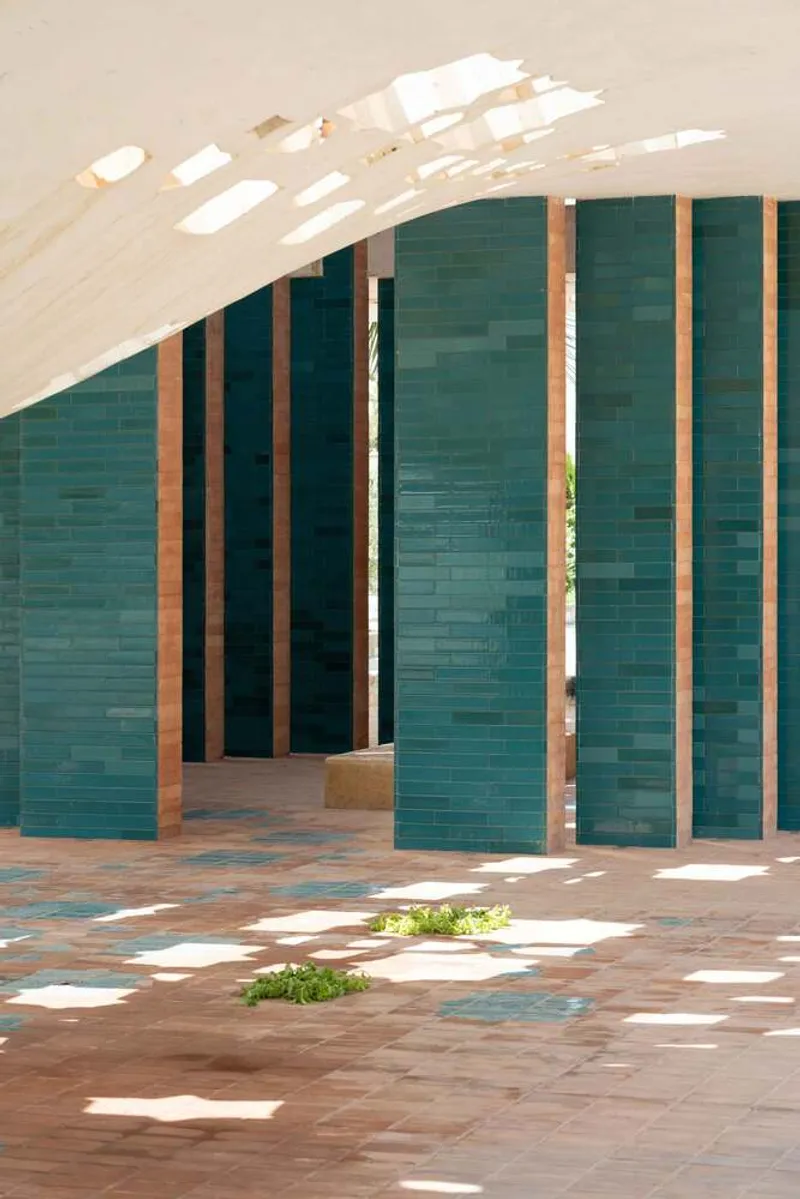 Vertical teal tile screen with timber framing under a perforated concrete vault casting dappled shadows