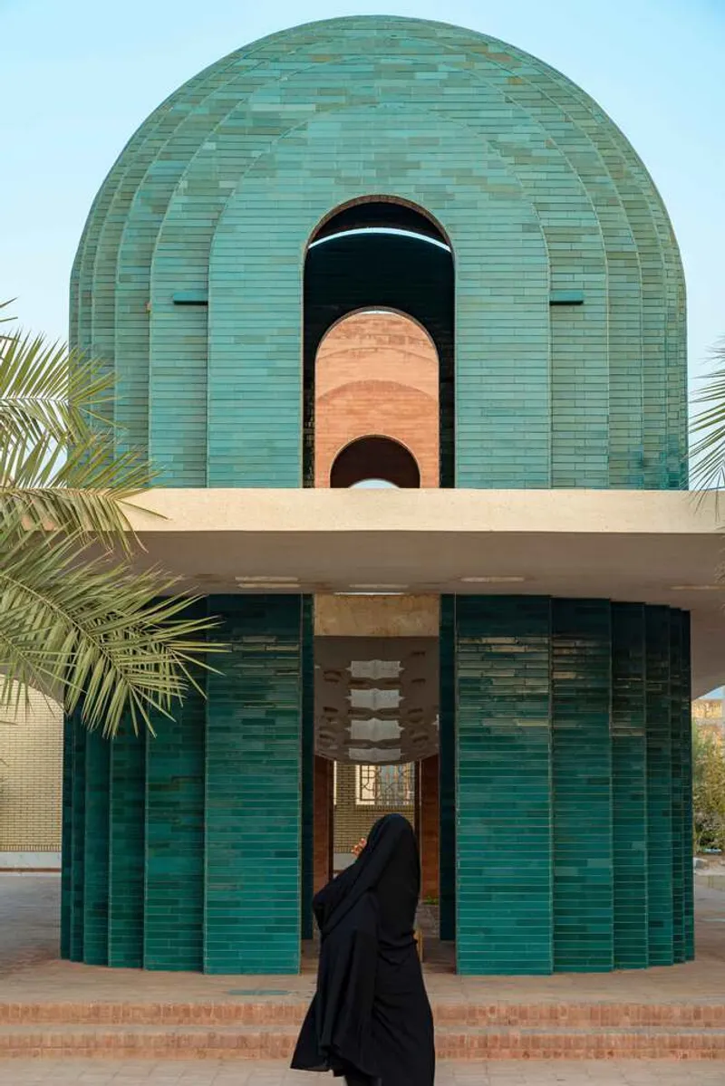 Frontal view of the layered teal and terracotta barrel vaults framed by palm fronds in daylight