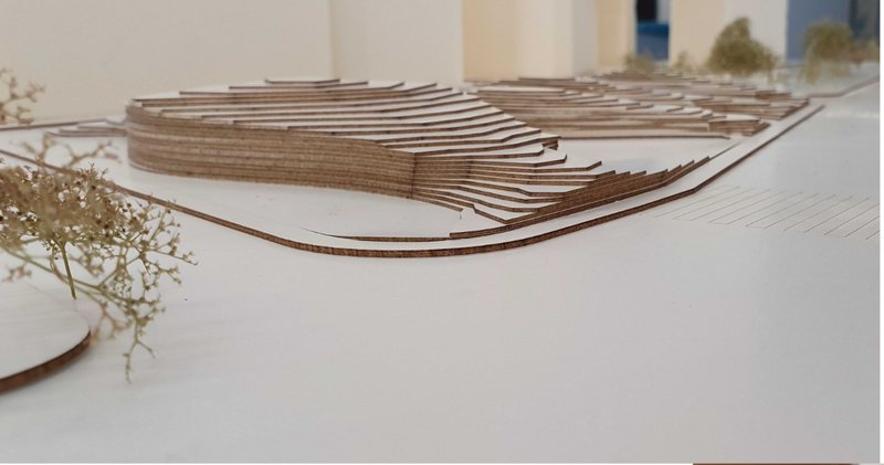 Physical model showing layered roof forms with curved profiles rising above a tree-planted base