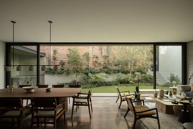 Dining room looking through full-height glazing to planted courtyard garden with brick wall beyond