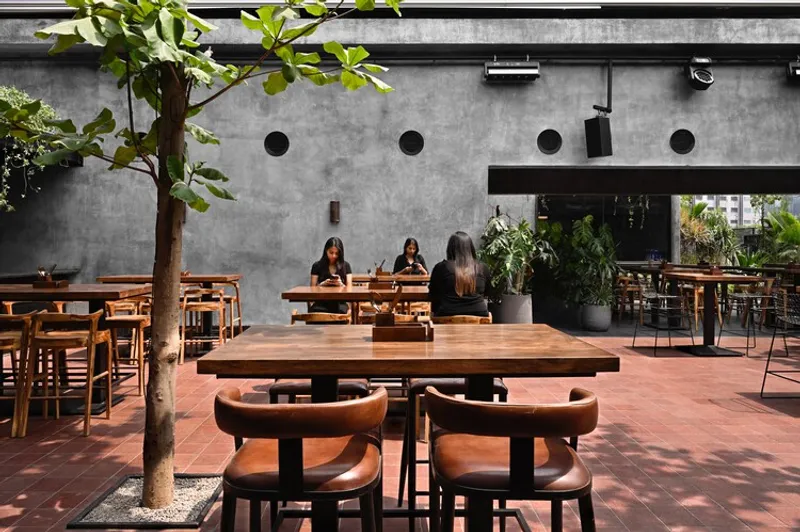 Open-air dining courtyard with concrete wall punctured by circular openings and a planted tree