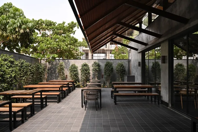 Covered outdoor courtyard with timber bench seating, steel frame roof and climbing plants along the concrete wall