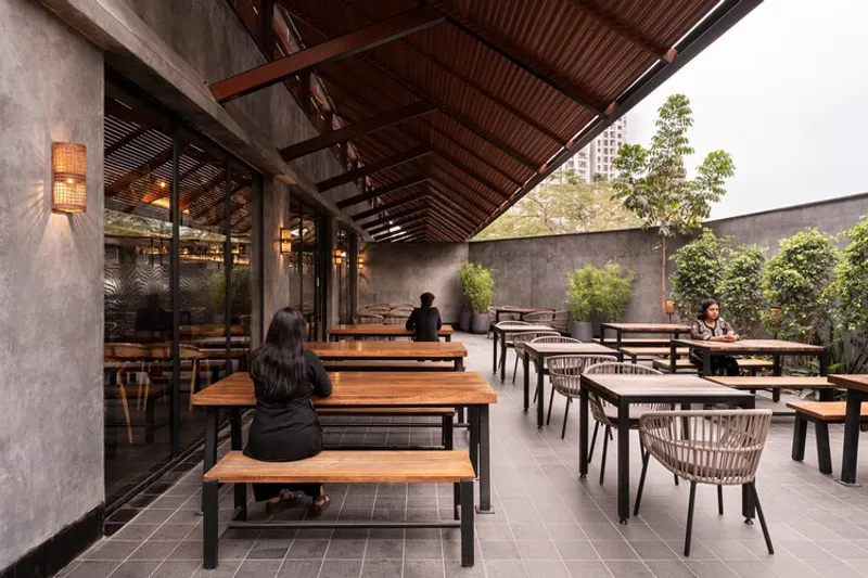 Open-air dining terrace with timber benches under a slatted wood ceiling and guests seated at tables
