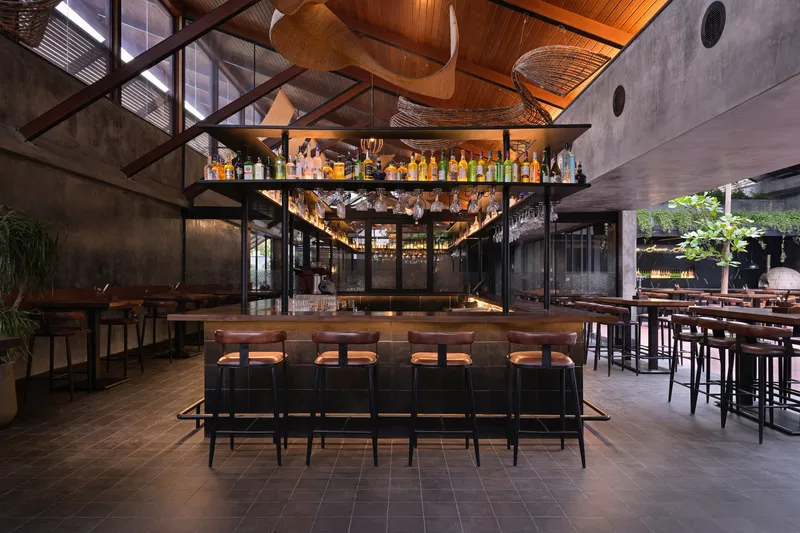Bar area with suspended glass shelving beneath woven timber ceiling and exposed steel trusses