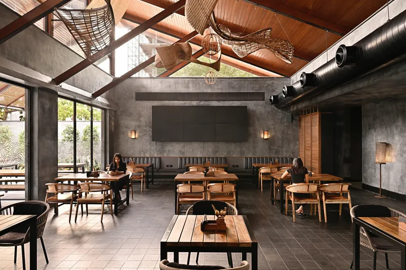 Dining hall with exposed timber trusses, concrete walls and patrons seated at wooden tables
