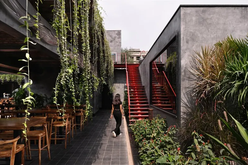 Exterior staircase with red treads flanked by concrete walls and trailing vines, person walking through