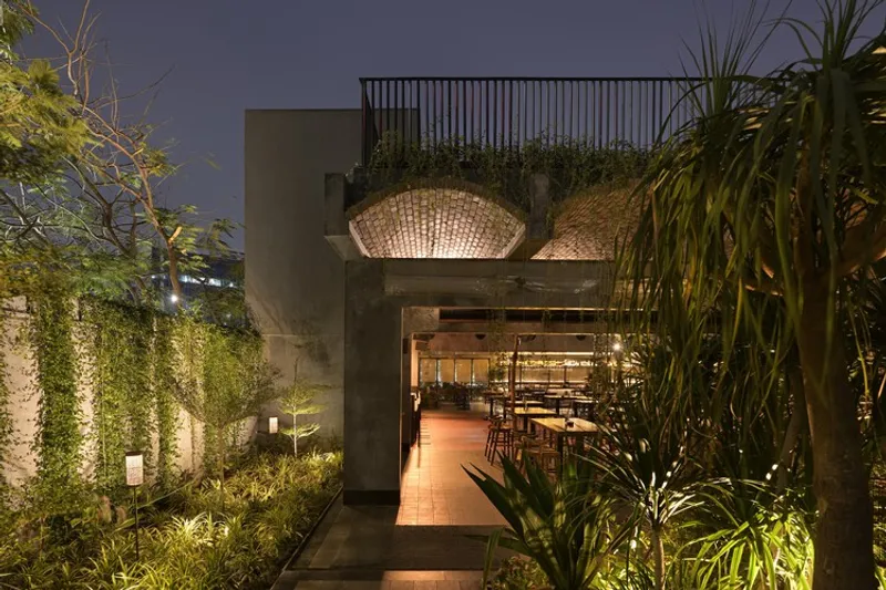Entrance pathway at dusk with uplighting through planted beds and woven basket lights hanging above the doorway