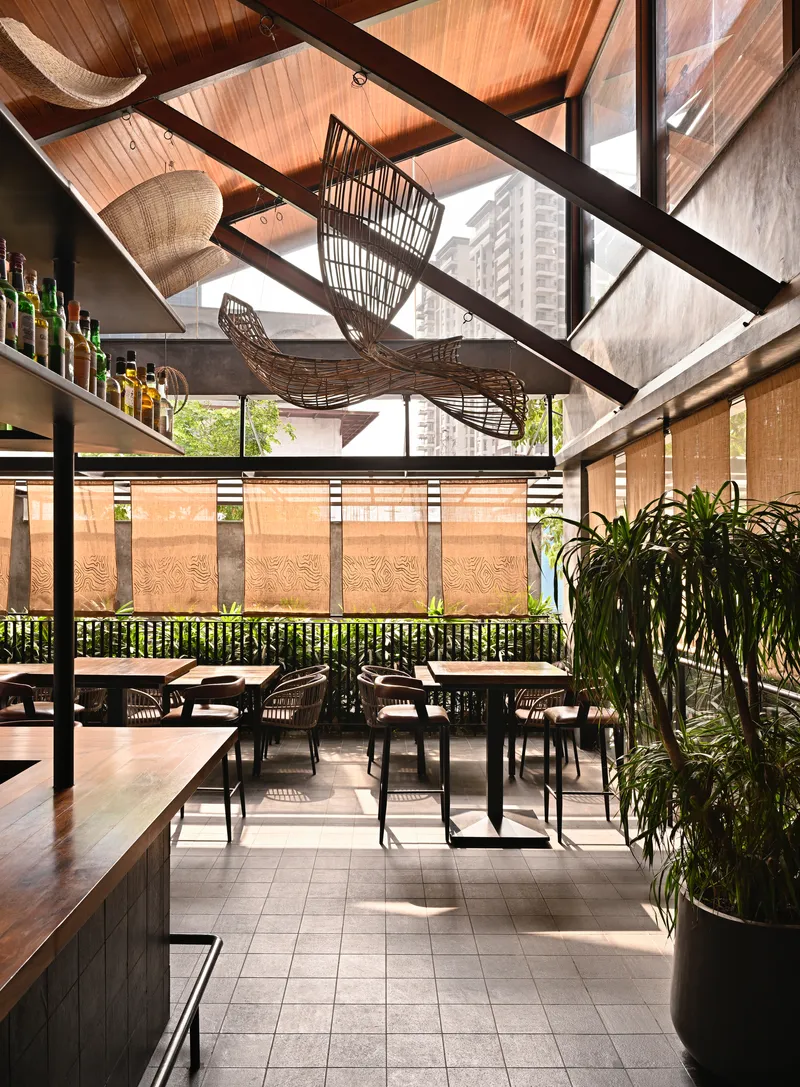 Dining space under a pitched timber ceiling with exposed steel trusses and woven basket chandeliers suspended overhead