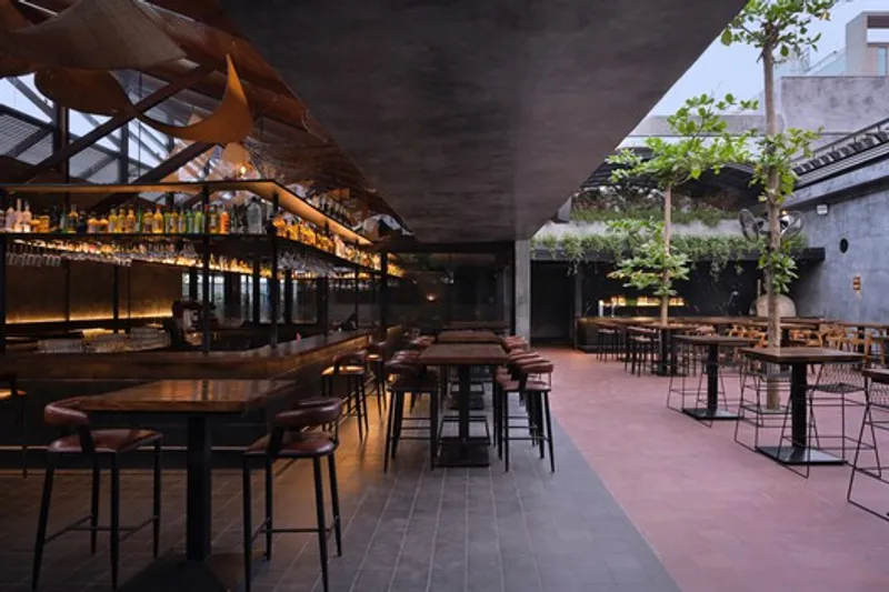 Bar area under concrete ceiling with illuminated bottle shelves at dusk