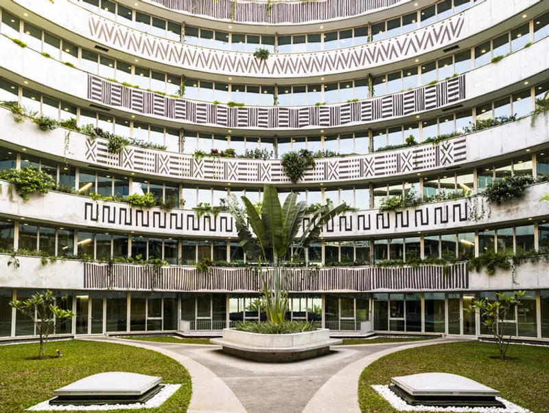 Curved courtyard facade with geometric patterned balconies and planted terraces around a central lawn and fountain