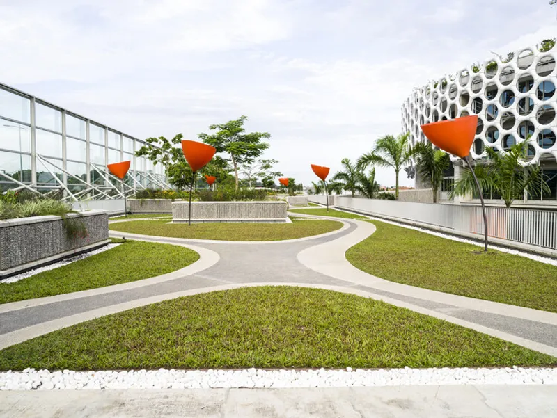 Curving pathways through terraced lawns with orange shade structures and palm trees under overcast skies