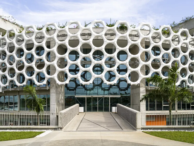 Ground level entrance with concrete ramp flanked by palms beneath the circular perforated facade screen