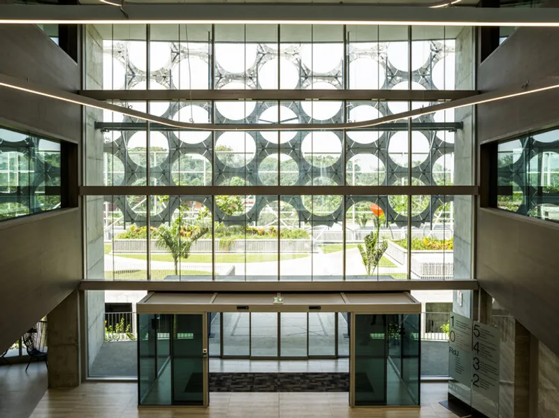 Triple-height atrium with full-height glazing revealing the patterned facade and landscaped grounds beyond