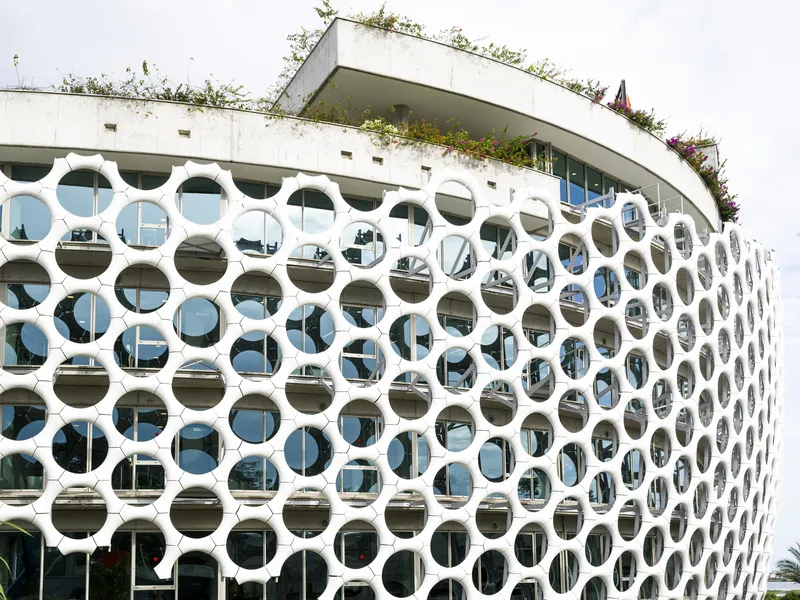 White precast circular screen facade with planted roof terrace above the curved glazed wall