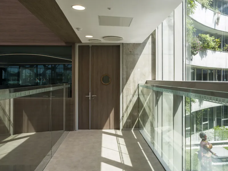 Glass-railed bridge connecting upper levels with sunlight streaming through windows onto concrete walls