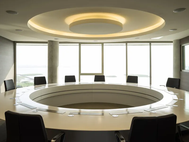Circular conference table with illuminated ceiling ring and windows overlooking a misty landscape