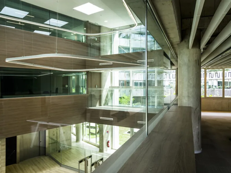 Multi-level interior atrium with glass railings, concrete columns, and timber flooring under skylights