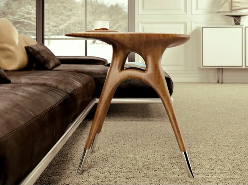 Sculptural wood side table with arched legs and tapered feet beside a leather sofa near a window