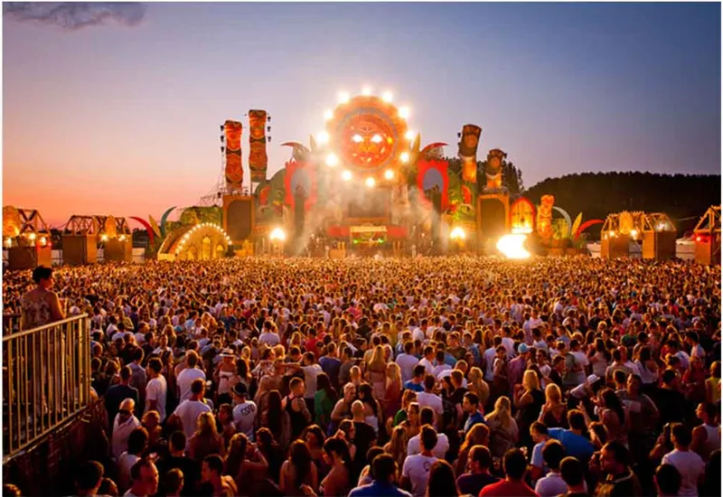 Illuminated stage structure with curved arched elements rising above a crowd at dusk