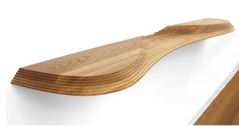 Close-up of a laminated timber shelf showing curved edges and layered grain detail against a white wall