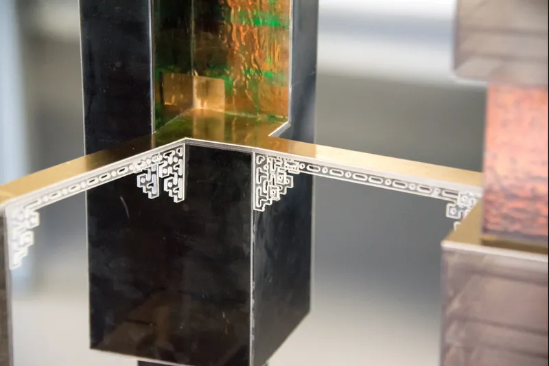 Close-up of a decorative corner bracket with geometric cutout pattern joining transparent model elements with gold accents