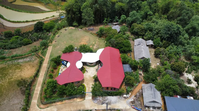Aerial view of the three-lobed red roof structure surrounded by green terraced fields and forest