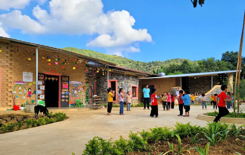 Courtyard with children playing outside the brick and stone classroom buildings under a blue sky