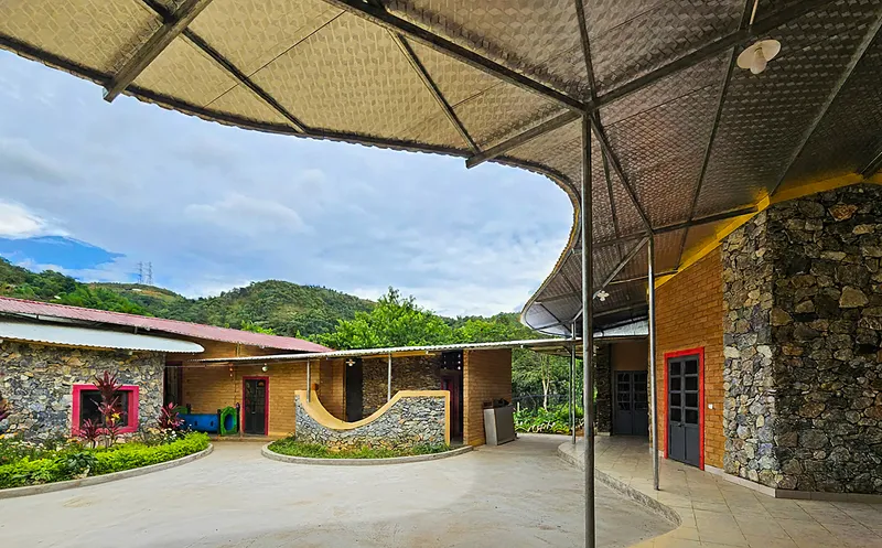 View from beneath the woven canopy showing curved stone and brick classroom wings facing the hills