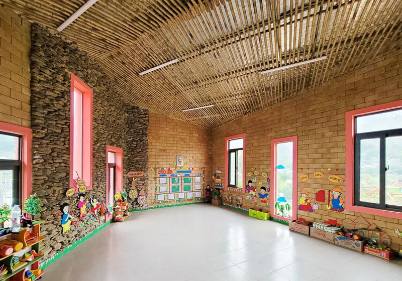 Interior classroom with bamboo slatted ceiling, exposed brick and stone walls, and pink window frames