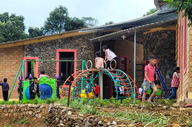 Low-pitched roof over stone and brick facade with children playing on playground equipment in front